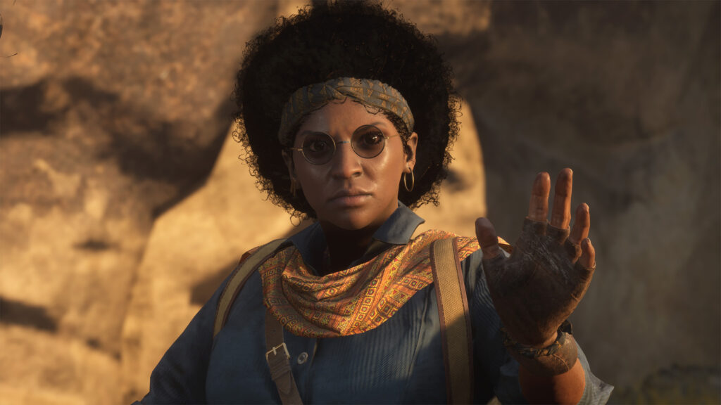 Buchra, in her signature sunglasses and Quaestor gear, holds up her hand in a scene from the Unknown 9: Awakening video game.